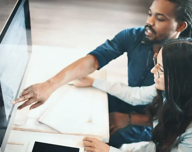 Two people working at a computer together while one points at the screen explaining